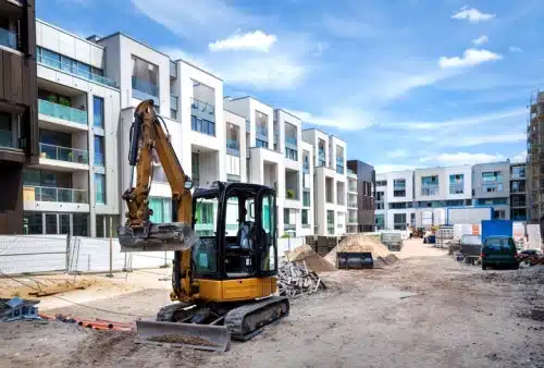 Baustelle mit Bagger vor modernen Wohnungen