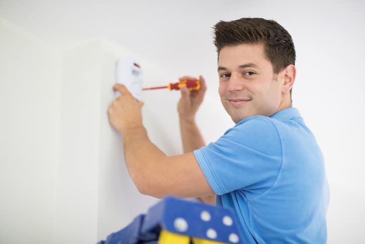 Elektroinstallateur arbeitet an Wandvorrichtung lächelnd